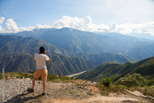Foto Unrecognizable young man seen from behind taking pictures of the Chicamocha Canyon, mountainous Andean scenery in Santander, Colombia under the morning sunlight