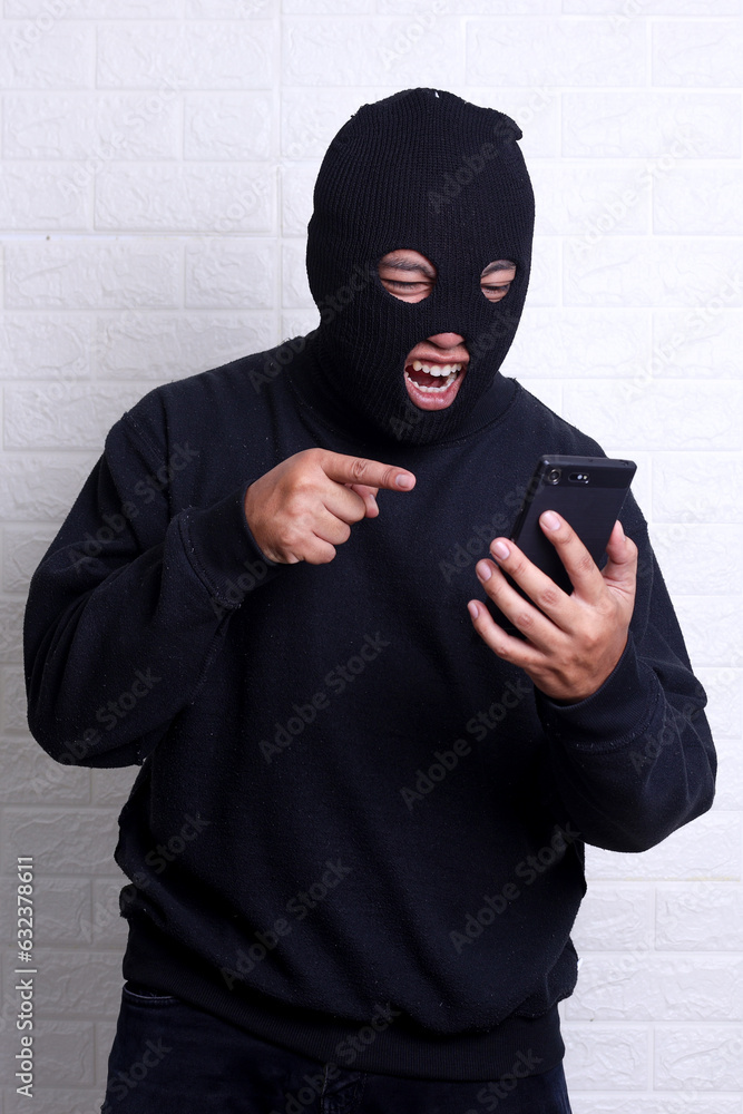A bad guy wearing balaclava trying to steal someone personal data using mobile phone A bad guy wearing balaclava trying to steal someone personal data using mobile phone