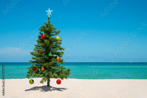 Christmas Tree on the beach. Merry Christmas. Happy New Year. Winter Holidays. Miami Florida vacation. Decorated Christmas pine or fir tree. Tropical Nature. Blue ocean on background with copy space © artiom.photo