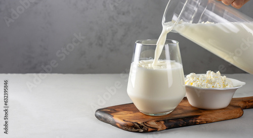 Kefir or Ayran fermented drink is poured into a glass from a jug, as well as cottage cheese in a bowl on a light gray background, Copy space, Close up photo