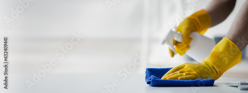 Person cleaning the room, cleaning staff is using cloth and spraying disinfectant to wipe the tables in the company office room. Cleaning staff. Maintaining cleanliness in the organization.