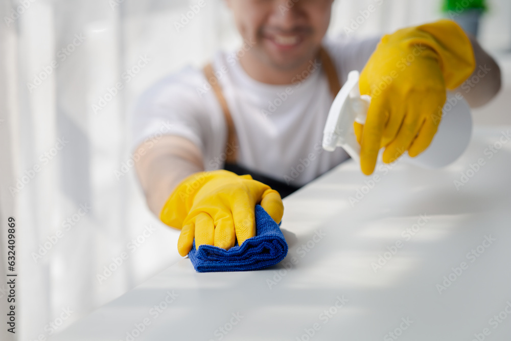 Person cleaning the room, cleaning staff is using cloth and spraying disinfectant to wipe the desk in the company office room. Cleaning staff. Maintaining cleanliness in the organization. Person cleaning the room, cleaning staff is using cloth and spraying disinfectant to wipe the desk in the company office room. Cleaning staff. Maintaining cleanliness in the organization.