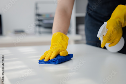 Person cleaning the room, cleaning staff is using cloth and spraying disinfectant to wipe the desk in the company office room. Cleaning staff. Maintaining cleanliness in the organization.