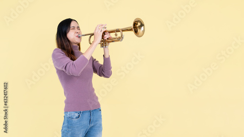 A beautiful and talented Asian woman is playing the trumpet, isolated yellow studio background