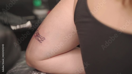 Man adding the finishing touches on a tattoo consisting of lines on the back side of the upper arm of a female customer. photo