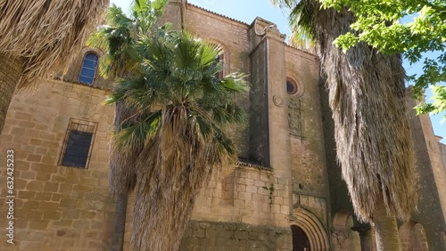 Establishing shot looking up at Iglesia de Santiago el Mayor medieval catholic parish church with lush palm trees foliage growing outside photo