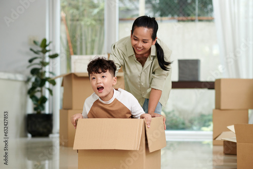 Mother pushing cardboard box with her son sitting inside