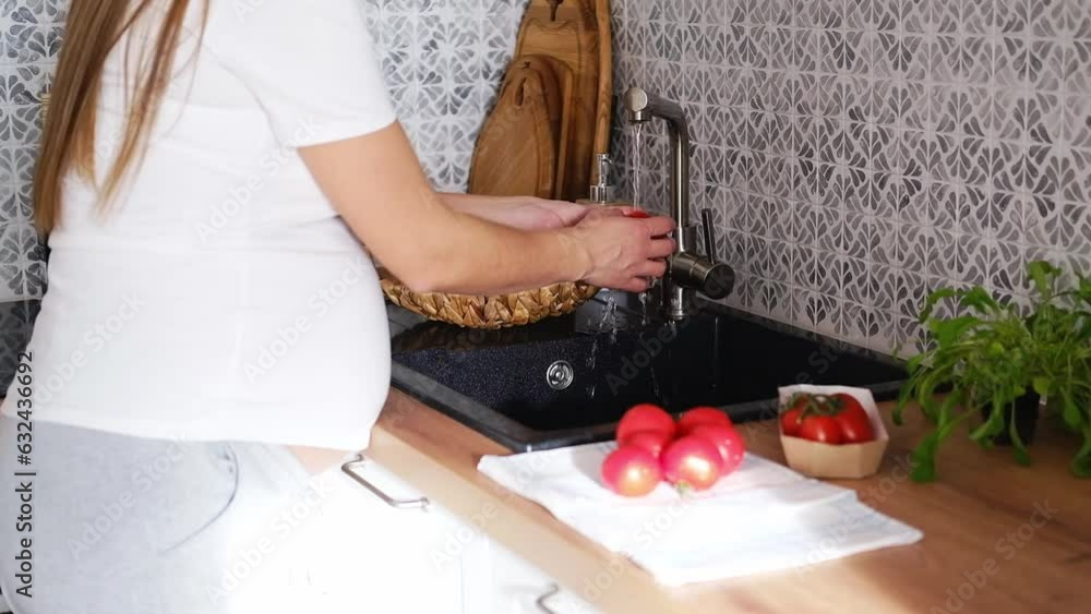 Close-up of a pregnant woman washing tomatoes in the sink in the kitchen Close-up of a pregnant woman washing tomatoes in the sink in the kitchen