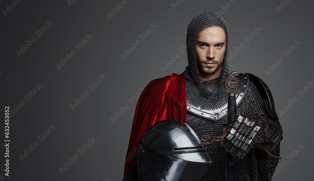 Portrait of a handsome king in heavy armor, chainmail, and steel crown, posing with a sword against a gray background Portrait of a handsome king in heavy armor, chainmail, and steel crown, posing with a sword against a gray background