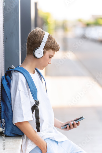 Boy with backpack using mobile phone and headphones outdoors. Technology concept.