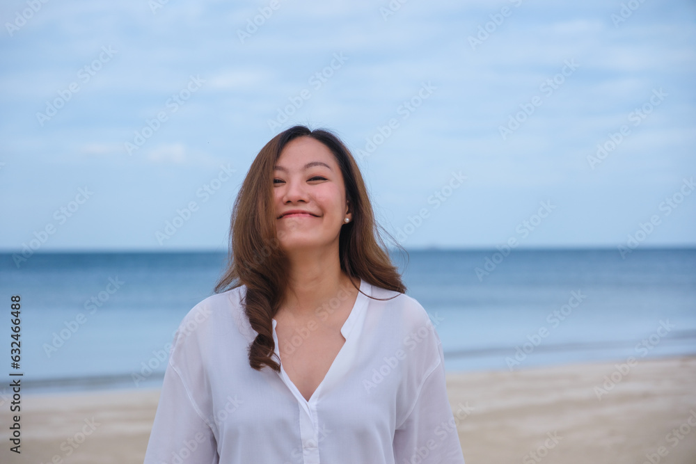 Portrait image of a beautiful young asian woman while strolling on the beach with the sea and blue sky Portrait image of a beautiful young asian woman while strolling on the beach with the sea and blue sky