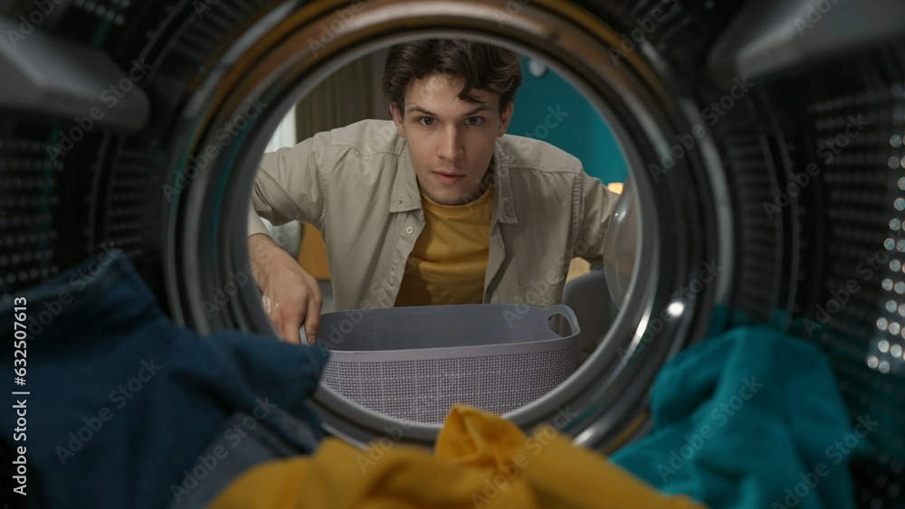 View from inside the washing machine, adult man with laundry basket takes out clothes from the drum View from inside the washing machine, adult man with laundry basket takes out clothes from the drum