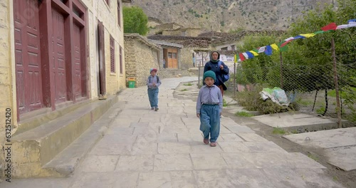 A woman brings her two kids to school in Mustang happily carrying their bag. Beautiful view from the alley of school and background scenario looks amazing 4K photo