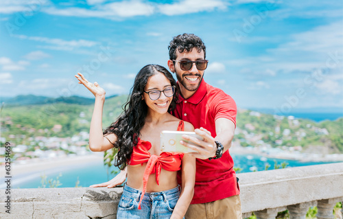 Smiling tourist couple taking a selfie at the viewpoint of San Juan del Sur. Happy Young tourist couple taking a selfie in a beautiful viewpoint photo