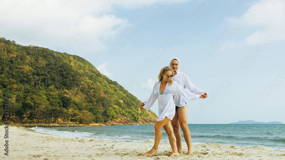 Cute loving couple in white dress, sunglasses, relax in hugging and kissing. Woman and man walk in beach. Concept sea beach resting tropical tourism summer holidays wedding love relationship vacation Cute loving couple in white dress, sunglasses, relax in hugging and kissing. Woman and man walk in beach. Concept sea beach resting tropical tourism summer holidays wedding love relationship vacation