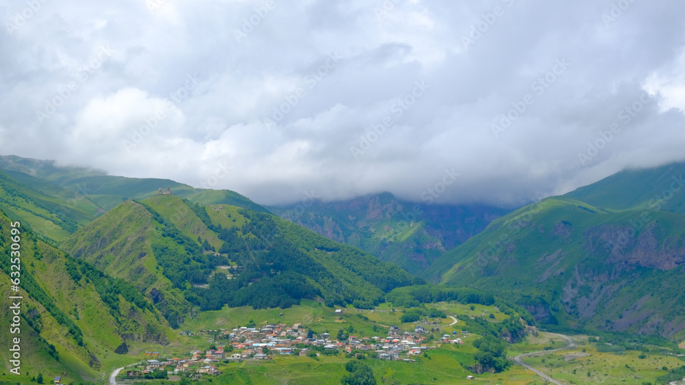 A View to Infinity: The Kazbegi Mountains Rise Above the Clouds, surrounding the small town of Kazbegi Mkinvartsveri in Georgia in a cloudy day in summer, Gudauri gergeti trinty church, ananuri