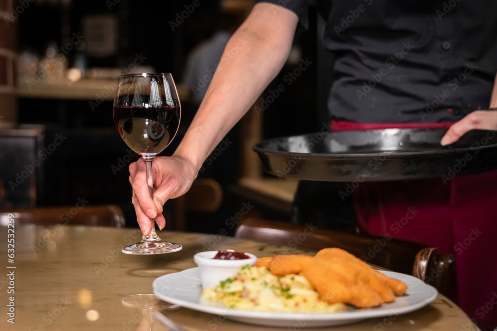 Kellnerin serviert Mann ein Schnitzel mit Beilagen und Rotwein im Restaurant 