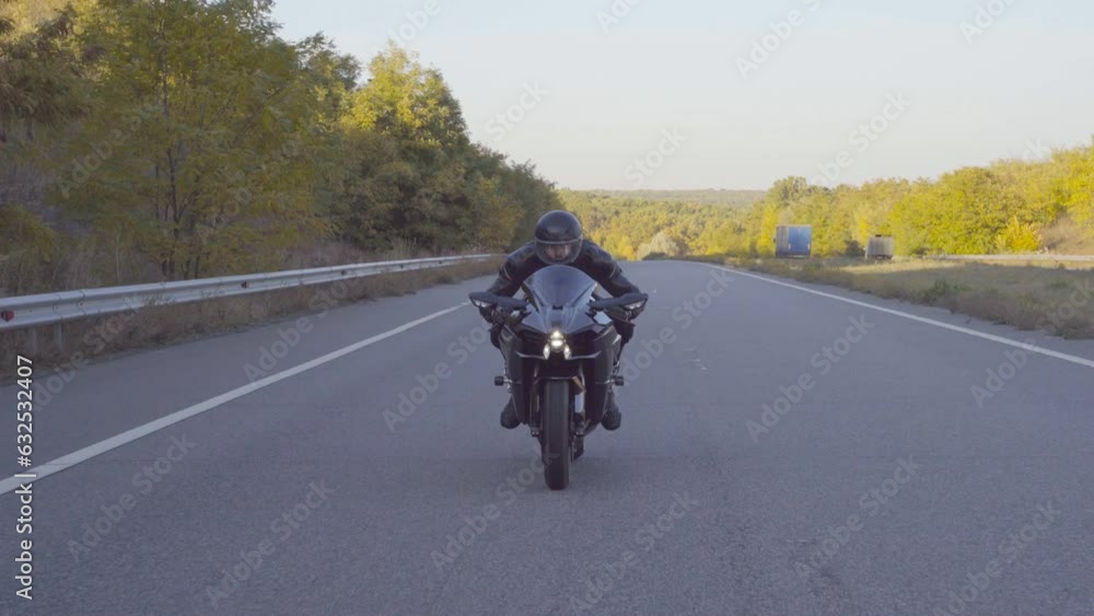 Front view of male biker in protective helmet riding fast on sport motorbike at highway. Motorcyclist moving on his bike at country road in early autumn. Young man driving motorcycle during trip Front view of male biker in protective helmet riding fast on sport motorbike at highway. Motorcyclist moving on his bike at country road in early autumn. Young man driving motorcycle during trip