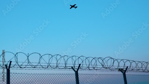 Airplane Flying In The Blue Sky With Razor Barbed Wire Fence In Warsaw Chopin Airport. - wide photo