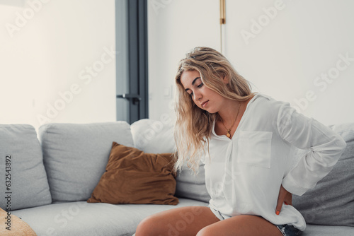 Close up tired woman suffering from backache, massaging back, sitting on sofa at home, frustrated girl feeling pain after long sitting in incorrect posture, touching loin, tensed muscles
 photo