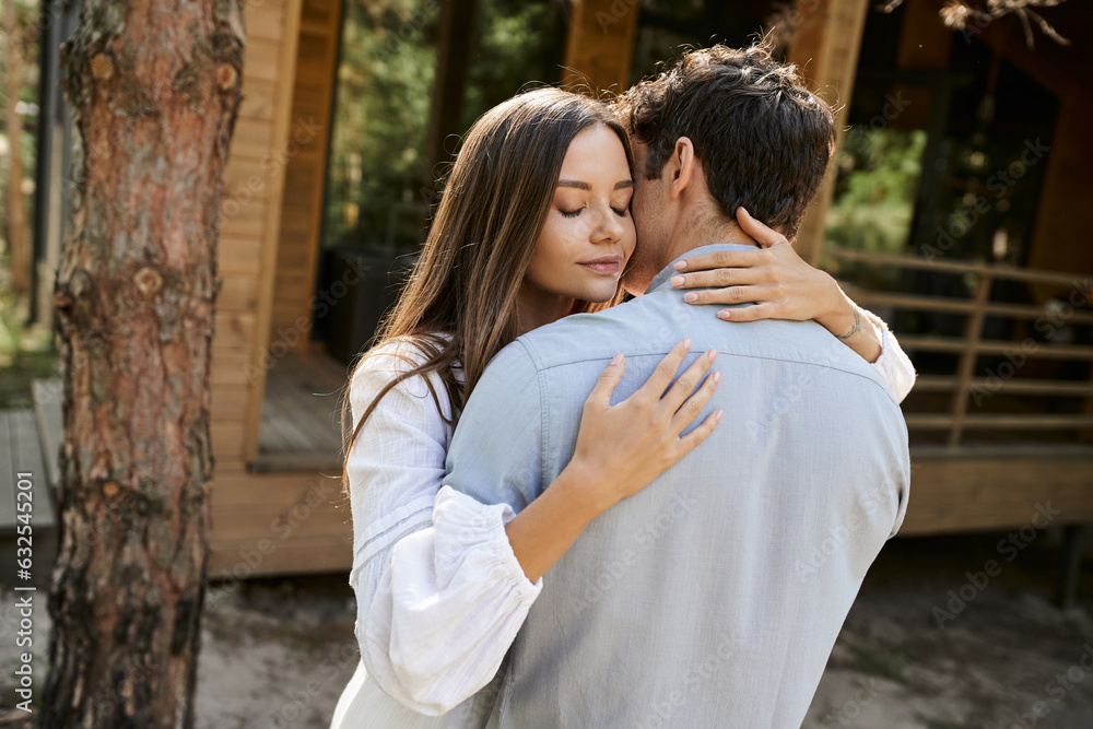 Brunette woman in sundress hugging boyfriend while standing near blurred vacation house outdoors Brunette woman in sundress hugging boyfriend while standing near blurred vacation house outdoors