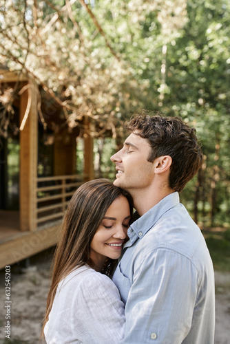 Smiling couple with closed eyes embracing and standing near vacation house at background outdoors © LIGHTFIELD STUDIOS