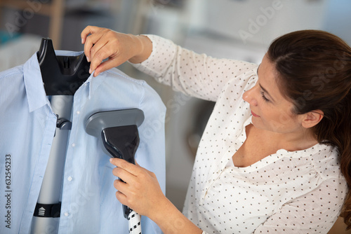 Fotografía woman with steamer cleaning clothes in dry-cleaning salon