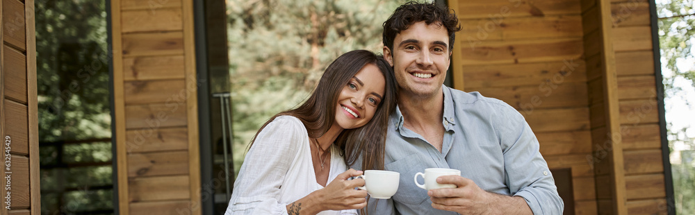 banner, cheerful couple holding cups of coffee, man and woman laughing on porch of vacation house banner, cheerful couple holding cups of coffee, man and woman laughing on porch of vacation house