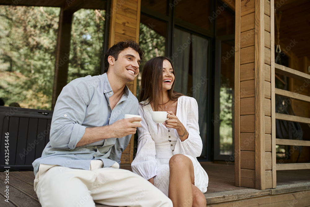 Φωτογραφία happy couple holding cups of morning coffee, man and woman laughing on porch of