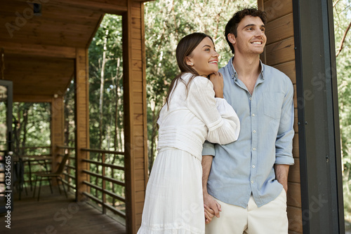 happy man standing with hand in pocket near beautiful woman in sundress, summer house, vacation