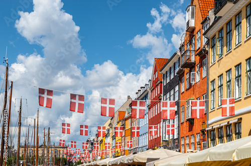 Waving danish flags above touristic street with colorful buildings in Nyhavn, Copenhagen in Denmark.