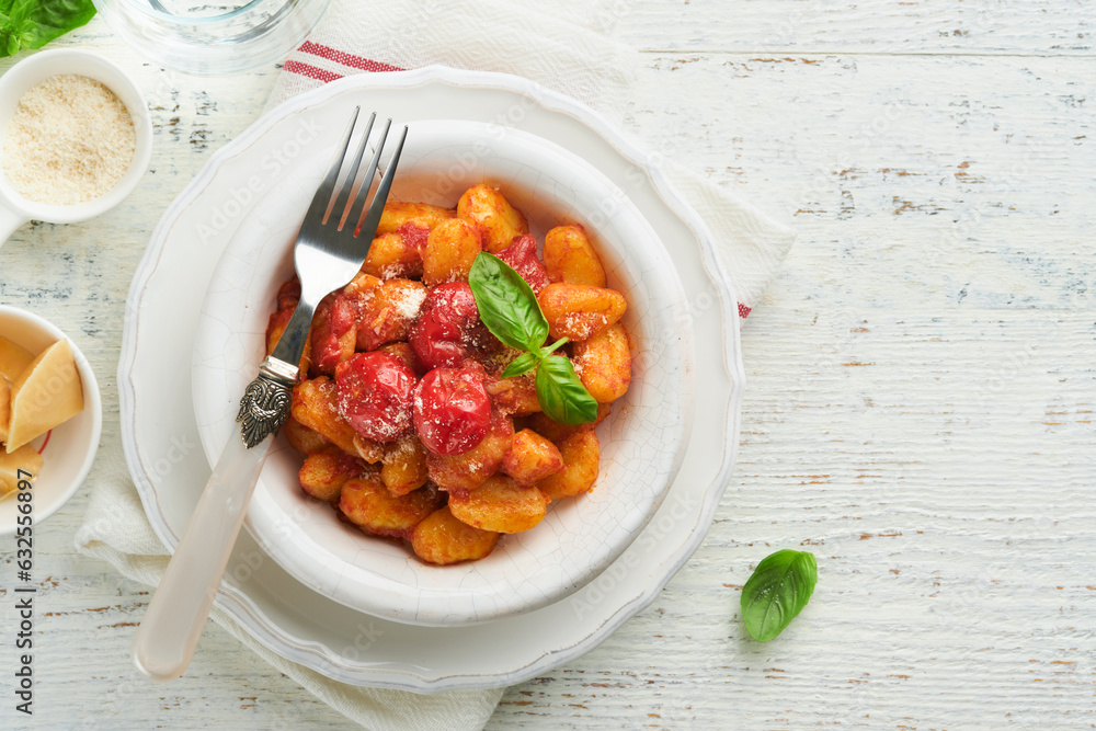 Potato gnocchi. Traditional homemade potato gnocchi with tomato sauce, basil and parmesan cheese on kitchen table on light grey kitchen table background. Traditional Italian food. Top view. Potato gnocchi. Traditional homemade potato gnocchi with tomato sauce, basil and parmesan cheese on kitchen table on light grey kitchen table background. Traditional Italian food. Top view.