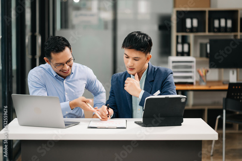 Two Asian business workers talking on the smartphone, tablet and using laptop at the office.
