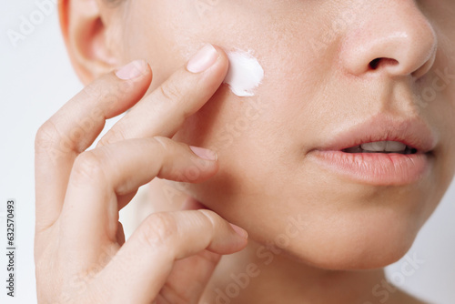 Tableau sur toile Close up of a young caucasian woman touching the face with her hand applying a smear of cream on the skin isolated on a white background