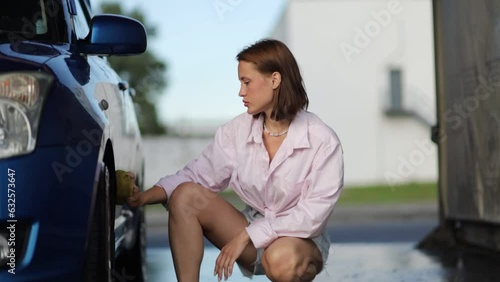 Beautiful woman washing the car with a sponge at the car wash.	 photo