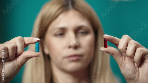 Close up shot of woman model holding blue and red capsules in her hands, showing it to the camera. Slow motion photo