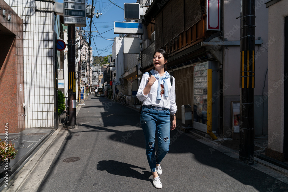 full length of amazed asian Taiwanese girl tourist having fun looking at old traditional Japanese houses while taking leisure walk on the street in downtown Kyoto japan