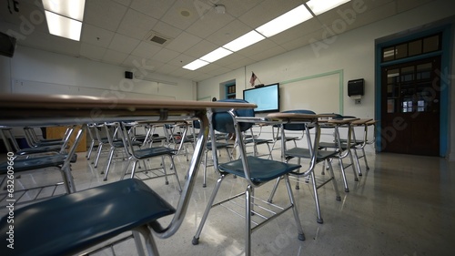 Empty classroom full of desks and chairs in a school with US flag and smart board.