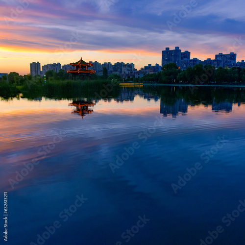In the city park, the beautiful sunset reflects the cloudy sky and the river surface of the lotus pond