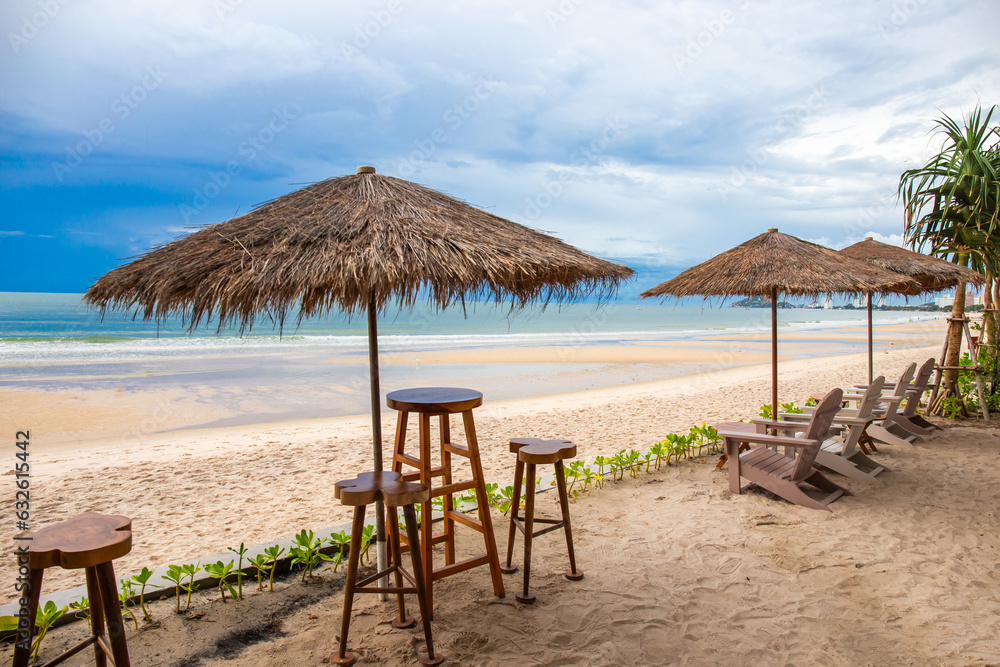 Set of wooden tables and chairs and leaf umbrellas for sitting and drinking drinks by the beach with sky and tide waves. Copy space background Set of wooden tables and chairs and leaf umbrellas for sitting and drinking drinks by the beach with sky and tide waves. Copy space background