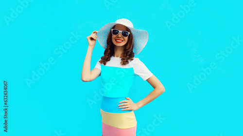 Beautiful young woman posing wearing summer straw hat, dress on blue studio background