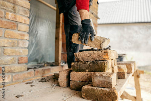 A builder is taking a brick from a pile on a building area.