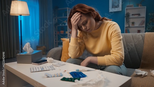 Unhappy woman sitting on the couch holding her head. A woman sadly looks at various medicines, blisters with pills. The woman is sick. Home medicine concept.