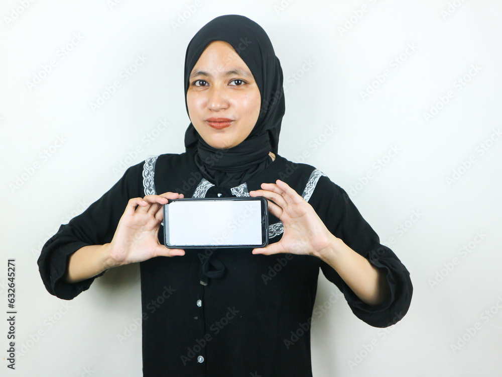 Young Muslim woman in hijab smiling showing mobile phone blank screen ...