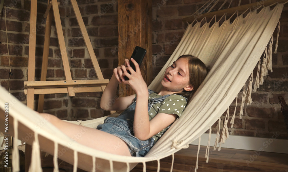 Preteen child girl lying in hammock in loft room at home. Pretty female kid enjoying summer vacation