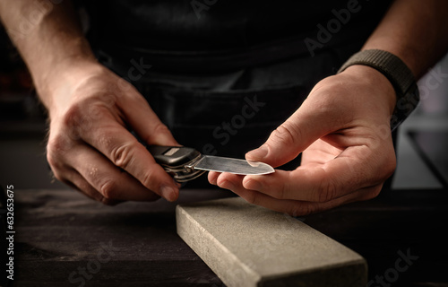 Man's hands with folding knife and sharpen stone tool. master sharpening penknife on a grindstone