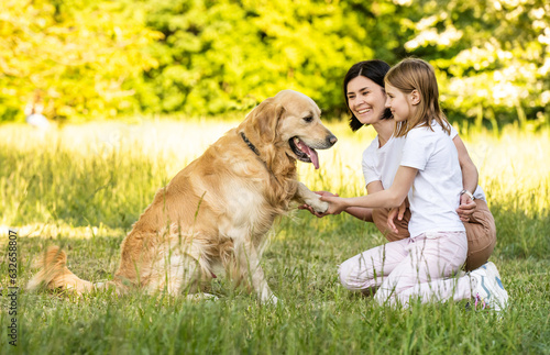 Mother and cute daughter playing with adorable golden retriever dog outdoors