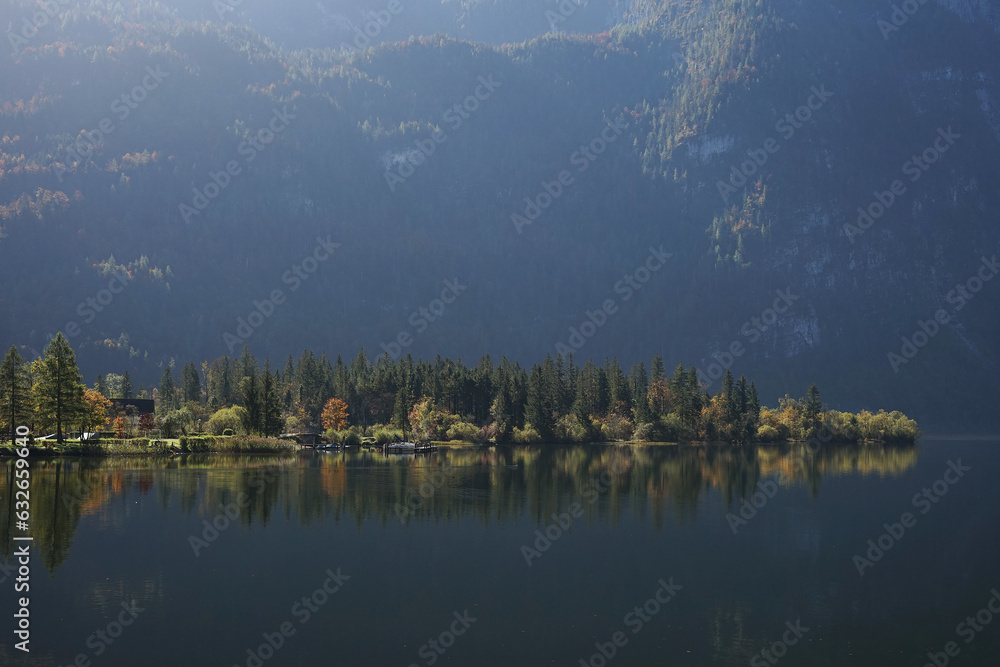 Fototapeta premium View of a mountain lake, a green shore with a forest and high mountains with morning sun rays