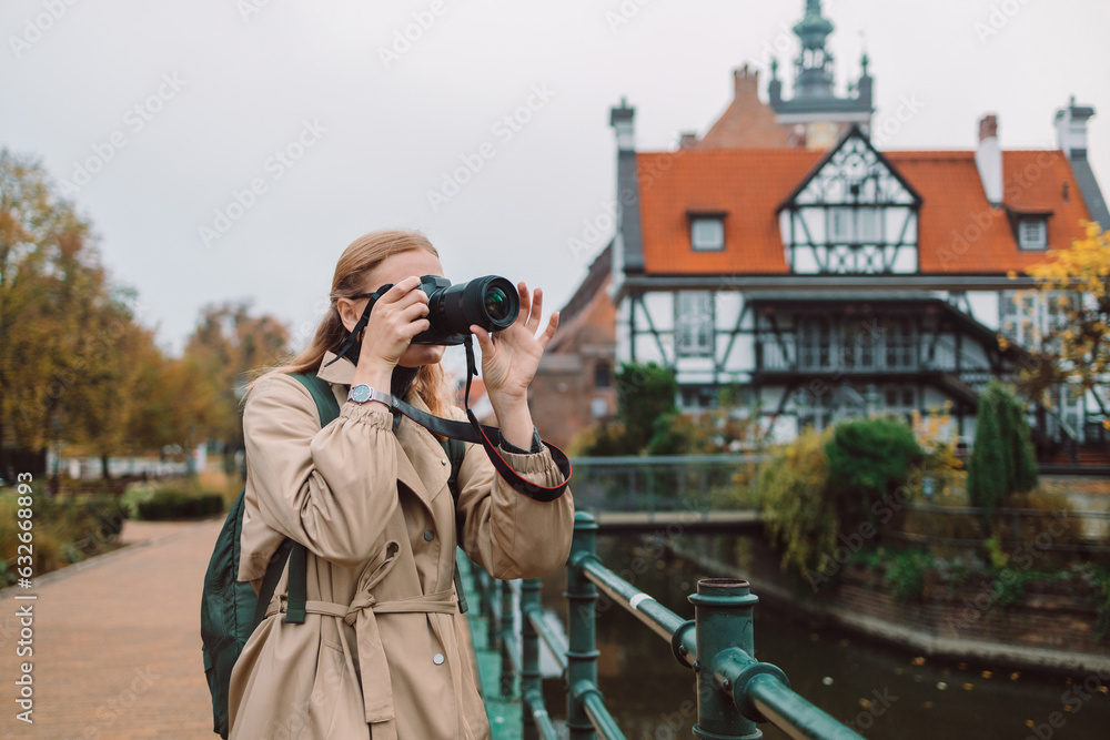 Real view of young European lady tourist in hat makes photo or video at city of Gdansk, Poland. High quality photo