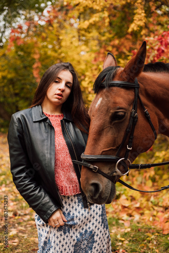 A beautiful young brunette kisses a horse. Autumn forest. Love for animals